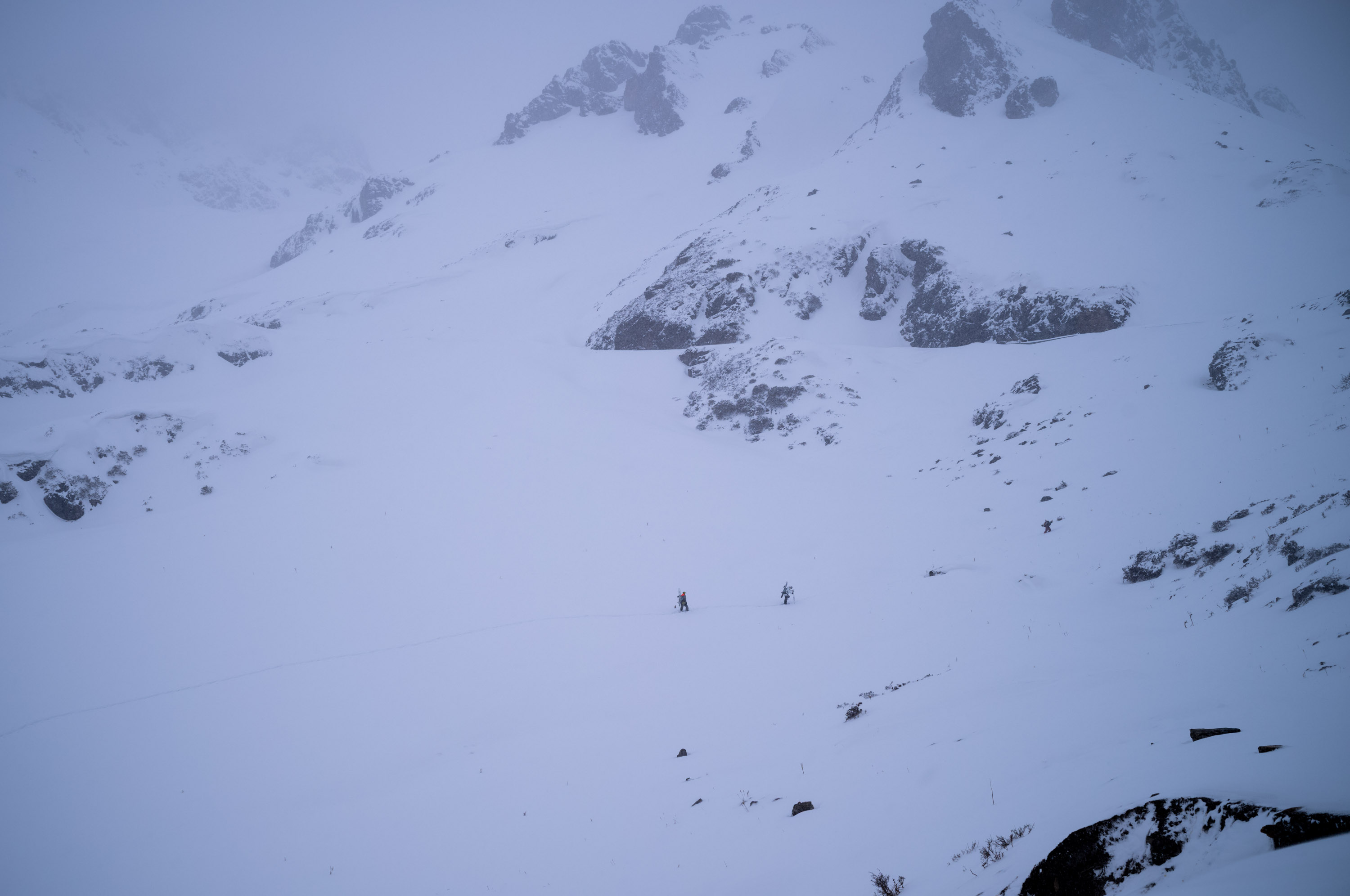 Three skiers descending through the valley. 山谷里有三个滑雪的人。
